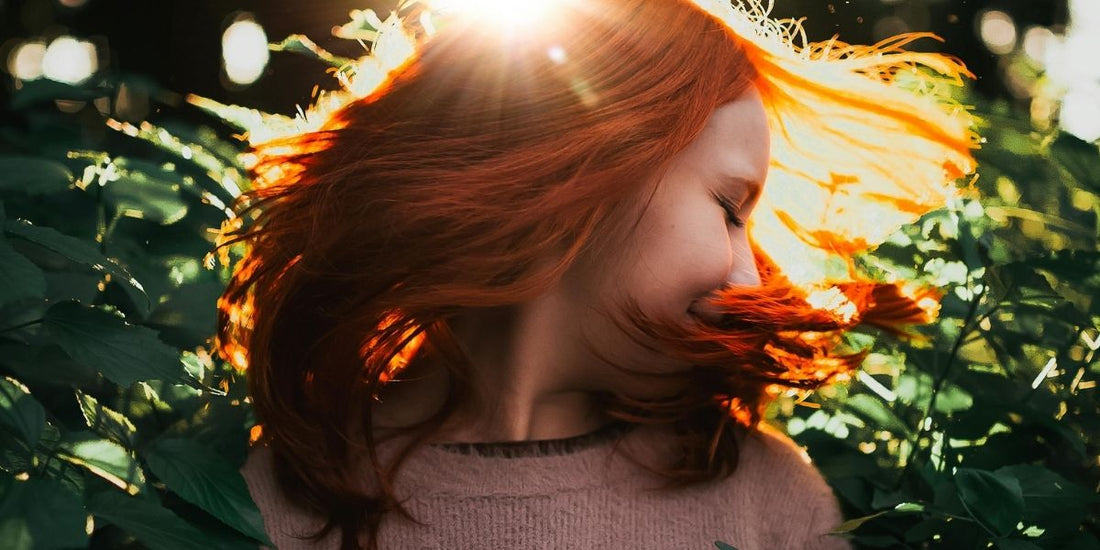 woman with red hear in sunlight and green foliage