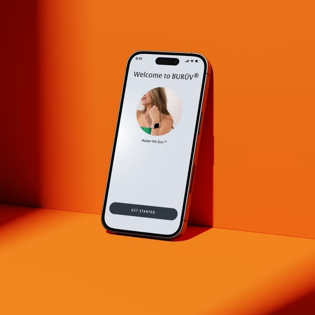 A smartphone stands upright against a bright orange background, displaying the BURŪV app login that reads 'Welcome to BURŪV' and 'Master the Sun.™'