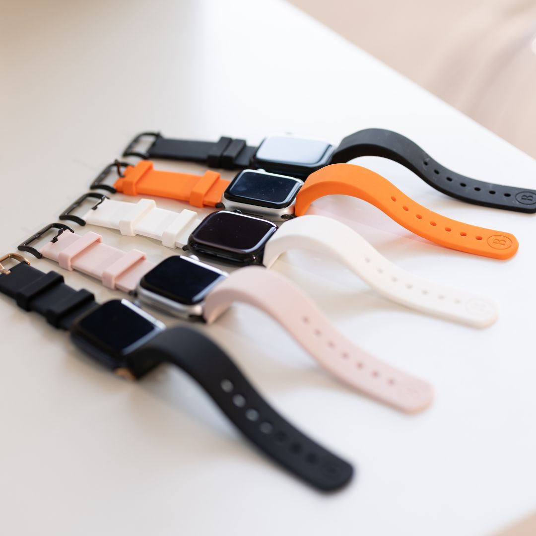 Five BURŪV smart bands: black, orange, white, blush, and black on a white counter.