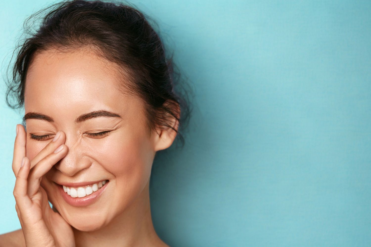 woman smiling behind hand with blue background