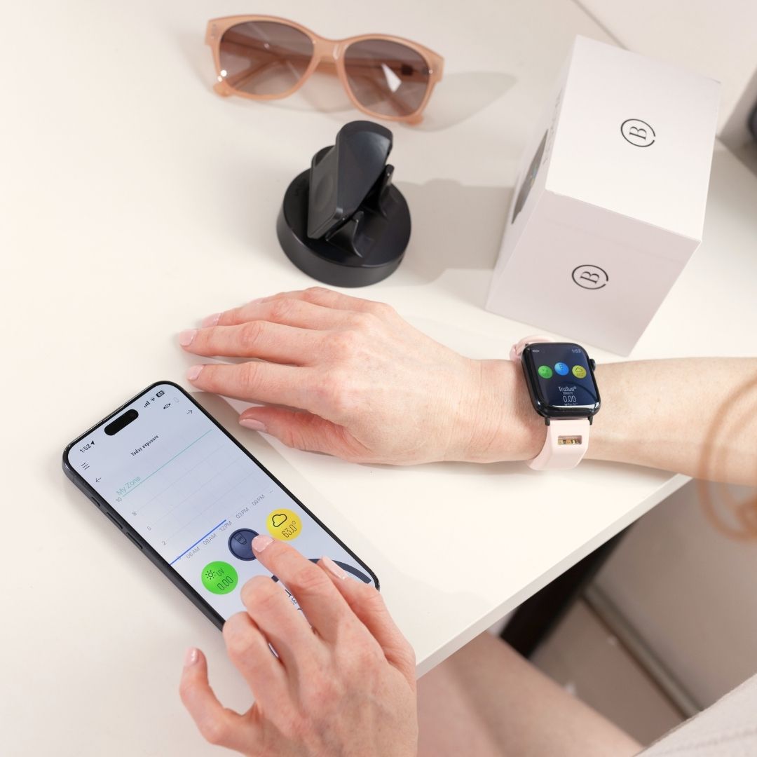 Woman setting up BURŪV® smart band for Apple Watch® using iphone on white desk
