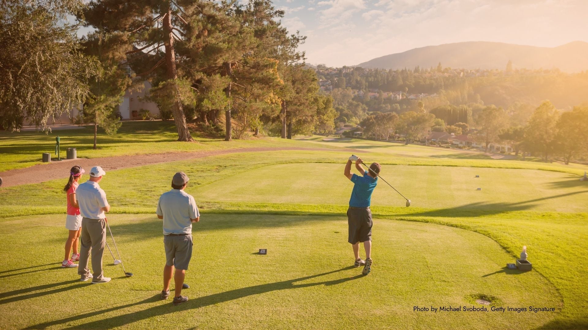 Golfers on a course with trees and mountains in the background