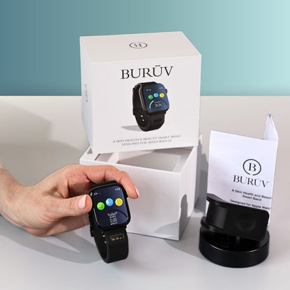 A hand holds a black BURŪV smart band for Apple Watch® in front of its white product box and charging dock on a light gray surface against a teal-blue background.