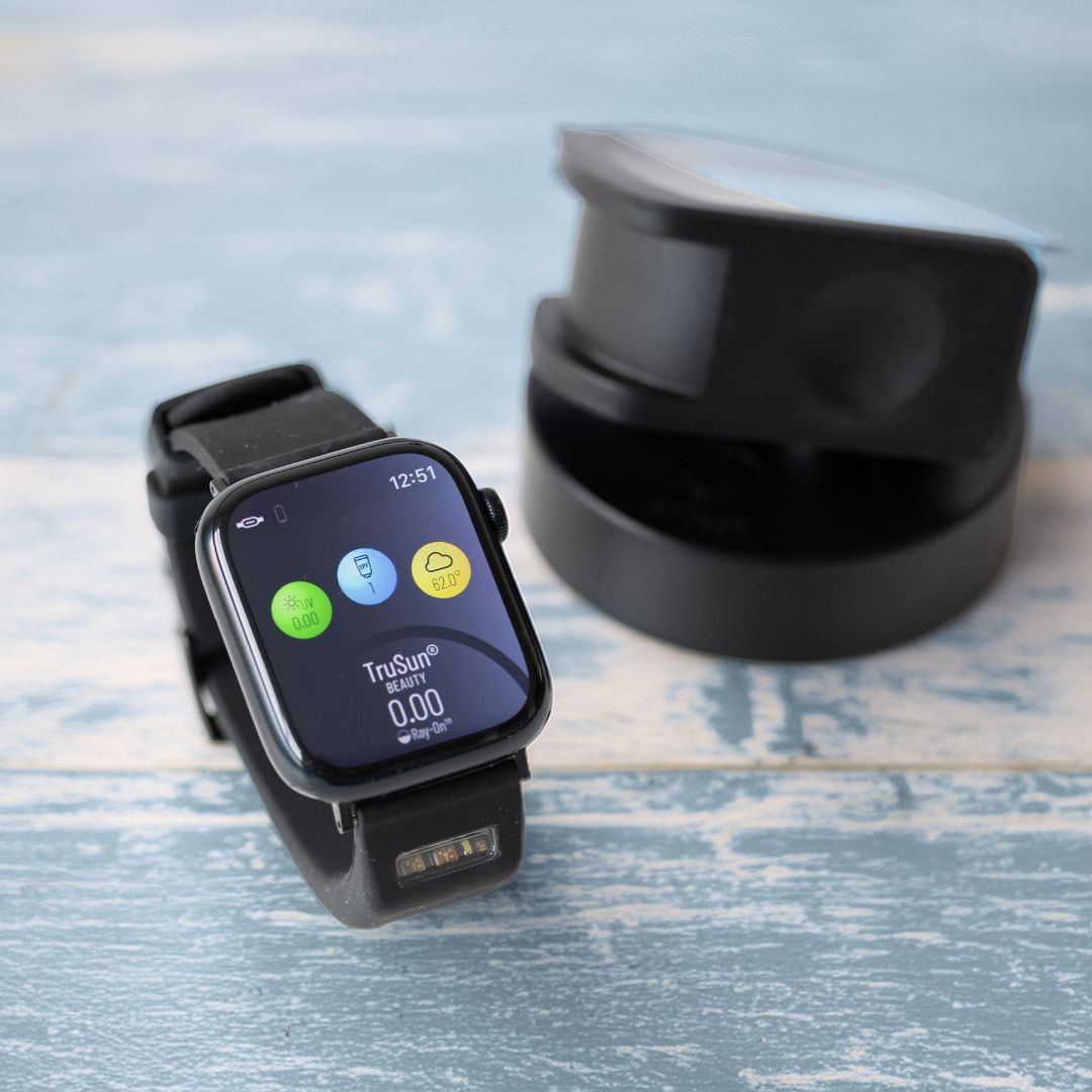 A black BURŪV smart band for Apple Watch® on a distressed blue wooden surface, with charging dock behind it.